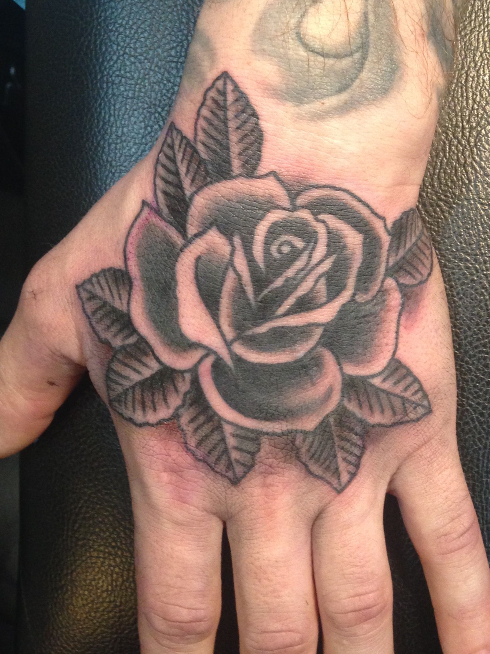 Black And Grey Hand Holding Flower Tattoo On The Arm